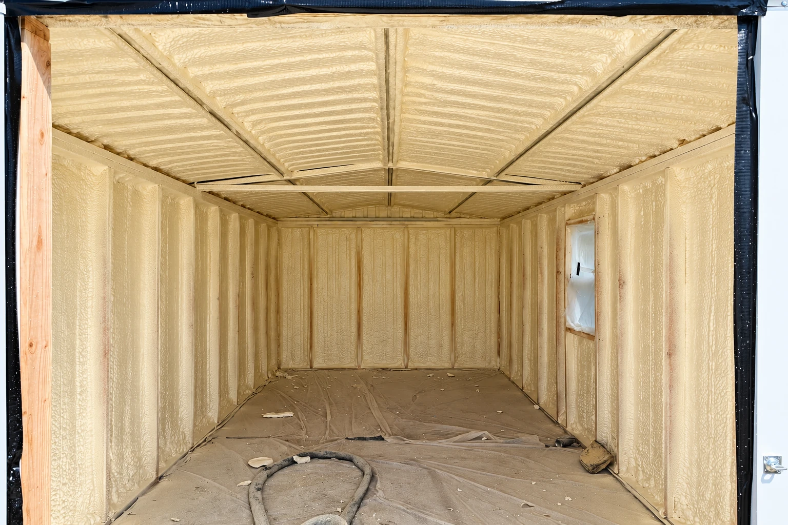 A bare framed room is fully coated with pale yellow spray foam across its walls and ceiling.