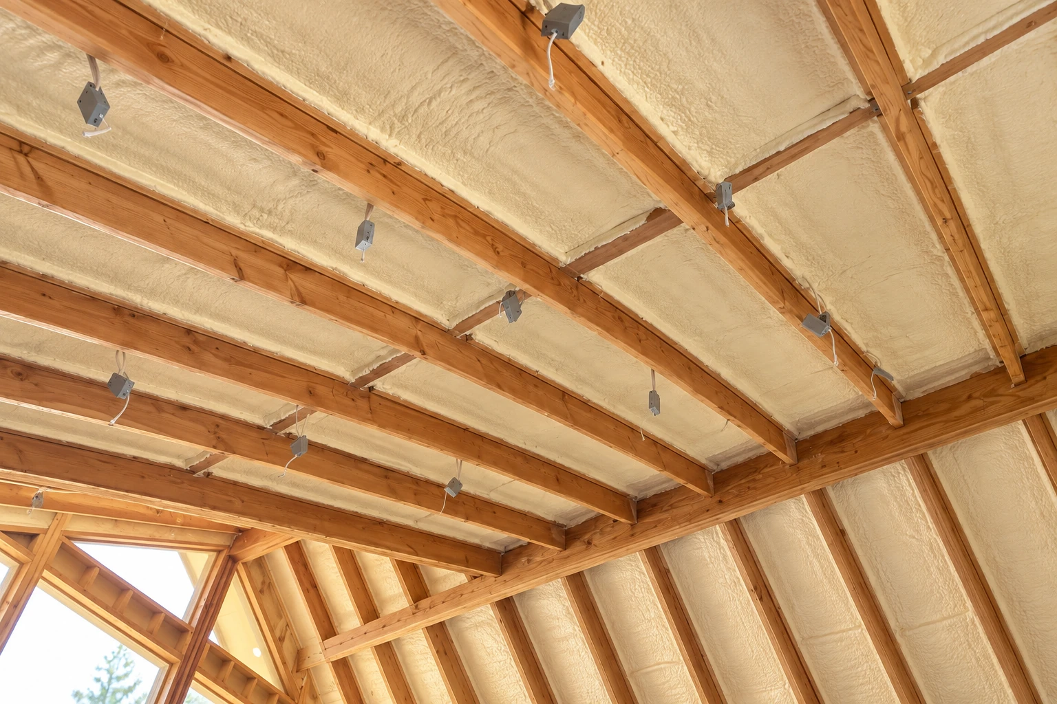 Open-cell spray foam fills the roof bays between exposed wooden rafters, with electrical boxes and loose wires visible.
