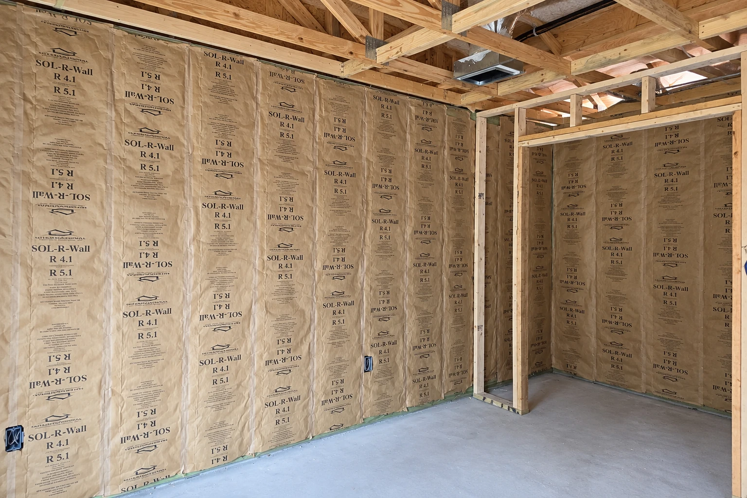 Fiberglass batts with brown paper facing fill the wall cavities of an unfinished room framed with exposed lumber.